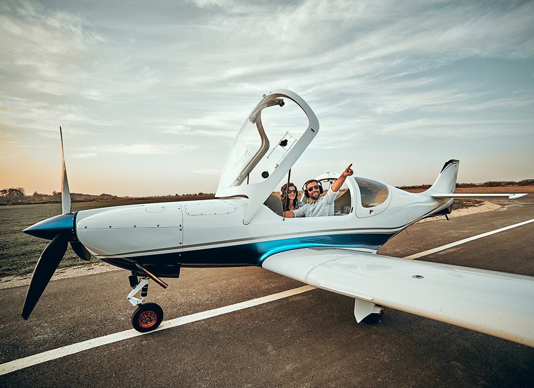 About Our Agency - Cheerful Young Couple Having Fun Sitting Inside a Private Two Passenger Plane at an Airport Looking Out at the Views Around Them