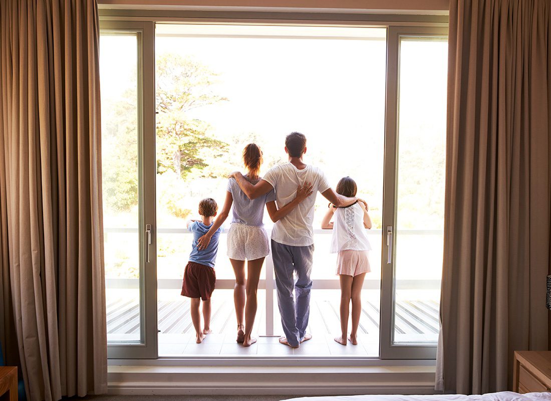 Personal Insurance - Rear View of a Family with Two Children Standing on a Balcony Outside a Bedroom in Their House on a Sunny Day Looking Out at the Garden