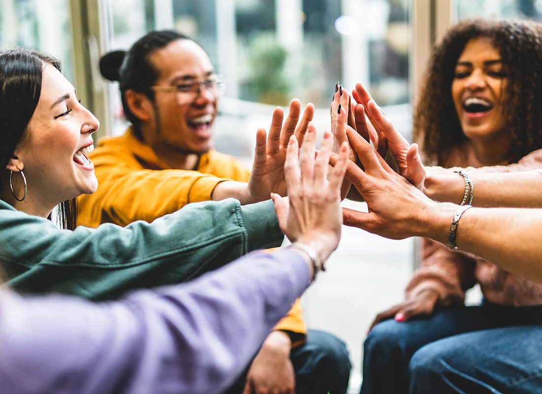 Read Our Reviews - Cheerful Group of Young Adults Putting Their Hands Together While Sitting in a Circle to Celebrate Success